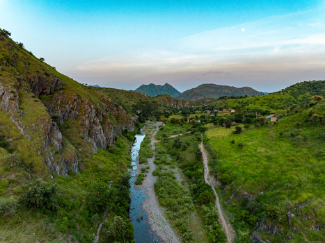 Aerial view of a winding river flowing through lush green hills and rocky terrain in the rural landscape of Udaipur Rajasthan India.