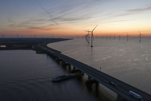 Aerial view of Ketelbrug bridge with a cargo ship passing underneath and wind turbines at sunset in Nagele Flevoland Netherlands.
