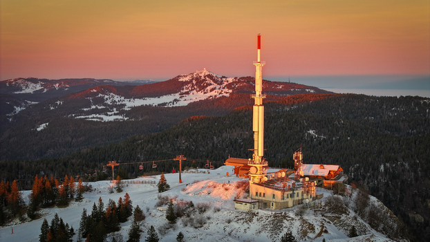Aerial view of the Col de la Faucille telecommunications tower and ski lifts on a snowy mountain peak during a vibrant sunset in Gex Auvergne Rhone Alpes France. Aerial view of the Col de la Faucille telecommunications tower and ski lifts on a snowy mountain peak during a vibrant sunset in Gex Auvergne Rhone Alpes France.
