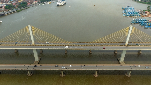 Aerial view of Atal Setu cable stayed bridge spanning the Mandovi River with vehicles driving across and fishing boats moored nearby in Panaji Goa India.