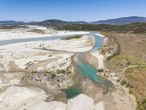 Aerial view of Vjosa Wild River National Park featuring turquoise river channels winding through white gravel riverbeds surrounded by hills in Permet Gjirokaster County Albania. Aerial view of Vjosa Wild River National Park featuring turquoise river channels winding through white gravel riverbeds surrounded by hills in Permet Gjirokaster County Albania.