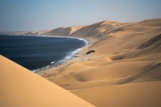 View of rolling golden sand dunes meet the deep blue sea under a clear sky creating a striking contrast in Anichab Erongo Namibia. View of rolling golden sand dunes meet the deep blue sea under a clear sky creating a striking contrast in Anichab Erongo Namibia.