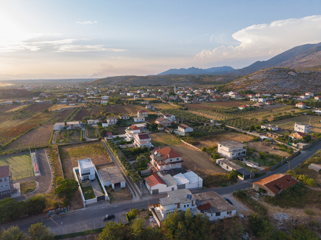 Aerial view of a rural landscape with scattered houses agricultural fields and roads under a soft sunset sky in Boks Qarku i Shkodres Albania.