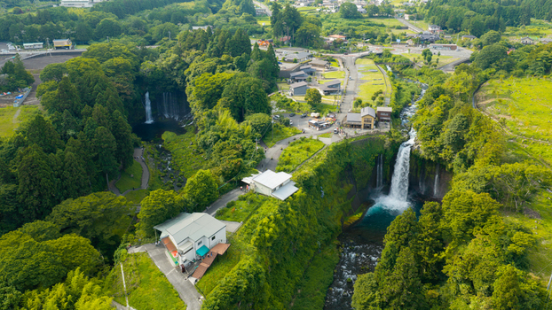 Aerial view of Shiraito Falls surrounded by lush green forest and buildings in Japan. Aerial view of Shiraito Falls surrounded by lush green forest and buildings in Japan.