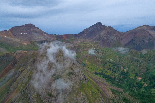 Aerial view of Mt. Sneffels and the rugged peaks of Yankee Boy Basin with mist clinging to the rocky slopes and lush green alpine meadows in Ouray Colorado United States.