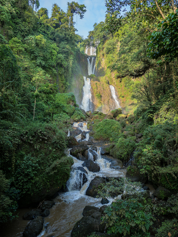Aerial view of the multi tiered Curug Telu via Kalices waterfall cascading through lush tropical forest and dark rocks in Kendal Central Java Indonesia. Aerial view of the multi tiered Curug Telu via Kalices waterfall cascading through lush tropical forest and dark rocks in Kendal Central Java Indonesia.