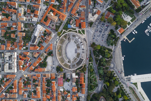 Aerial view of Pula Arena surrounded by historic stone buildings red tiled rooftops and the nearby Adriatic Sea coastline in Pula Istarska zupanija Croatia. Aerial view of Pula Arena surrounded by historic stone buildings red tiled rooftops and the nearby Adriatic Sea coastline in Pula Istarska zupanija Croatia.