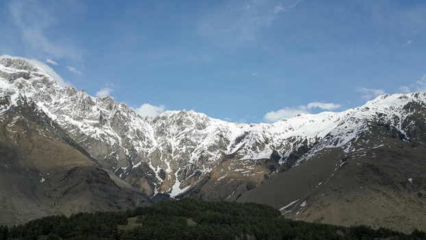 Aerial view of the snow covered Caucasus Mountains with rocky peaks patches of snow and a dense pine forest at the base under a clear blue sky in Georgia. Aerial view of the snow covered Caucasus Mountains with rocky peaks patches of snow and a dense pine forest at the base under a clear blue sky in Georgia.