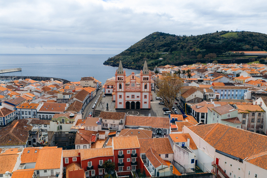 Aerial view of the historic Se Catedral de Angra do Heroismo surrounded by orange tiled rooftops and the coastal bay with Monte Brasil in the background in Angra do Heroismo Azores Portugal.