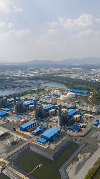 Aerial view of the Gulf PD Power Plant industrial complex featuring blue roofed buildings cooling towers and storage tanks under a hazy sky in Map Yang Phon Rayong Thailand.