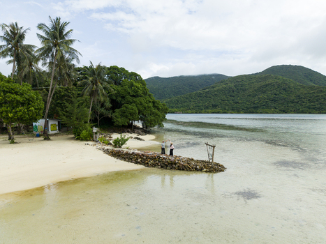 Aerial view of the tranquil Bobby Beach where white sand meets clear blue water contrasting with lush green vegetation and two girls playing together Karimunjawa Central Java Indonesia.