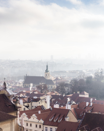 View of red tiled rooftops and a historic church tower under a misty sky in the old town district of Prague Prague Czechia. View of red tiled rooftops and a historic church tower under a misty sky in the old town district of Prague Prague Czechia.