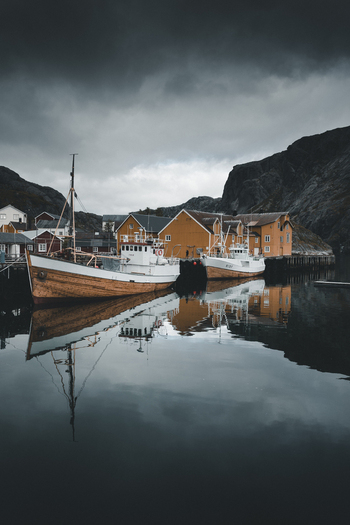 Nusfjord Nordland Norway 07 September 2022 View of historic Nusfjord with yellow wooden buildings and fishing boats moored in the calm harbor under a cloudy sky. Nusfjord Nordland Norway 07 September 2022 View of historic Nusfjord with yellow wooden buildings and fishing boats moored in the calm harbor under a cloudy sky.