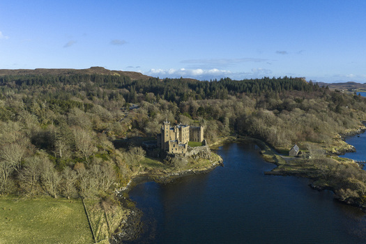 Aerial view of Dunvegan Castle and Gardens a historic stone fortress on a rocky promontory overlooking the water surrounded by dense woodland Isle of Skye Scotland United Kingdom. Aerial view of Dunvegan Castle and Gardens a historic stone fortress on a rocky promontory overlooking the water surrounded by dense woodland Isle of Skye Scotland United Kingdom.
