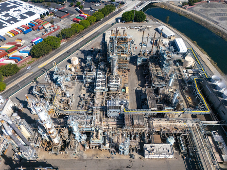 Aerial view of an industrial oil refinery facility with complex piping storage tanks and cooling towers located near a canal and shipping yard in Carson California United States.