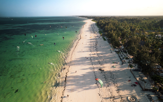 Aerial view of the stunning contrast between the turquoise waters teeming with kitesurfers and the pristine white sands bordering lush green trees Paje Unguja South Region Tanzania. Aerial view of the stunning contrast between the turquoise waters teeming with kitesurfers and the pristine white sands bordering lush green trees Paje Unguja South Region Tanzania.