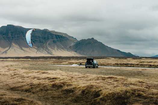 View of a person kiteboarding in a river with a parked car nearby against a backdrop of mountains in Borgarbyggd Iceland. View of a person kiteboarding in a river with a parked car nearby against a backdrop of mountains in Borgarbyggd Iceland.