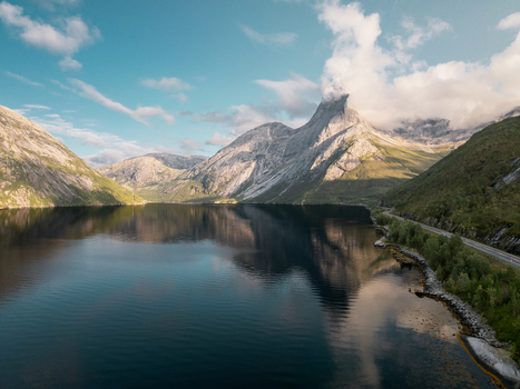 Aerial view of the iconic Stetind mountain rising above a calm fjord with a coastal road winding along the shoreline in Kjopsvik Nordland Norway. Aerial view of the iconic Stetind mountain rising above a calm fjord with a coastal road winding along the shoreline in Kjopsvik Nordland Norway.