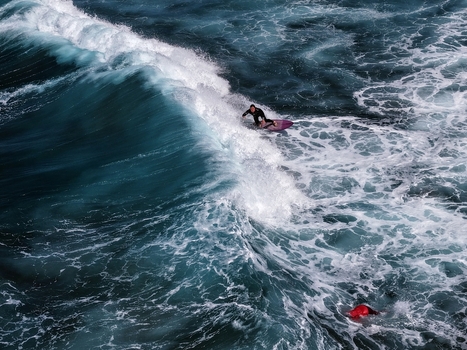 Aerial view of a surfer riding a powerful wave with white foam and deep blue water at Praia do Areal de Santa Barbara Ribeira Grande Acores Portugal. Aerial view of a surfer riding a powerful wave with white foam and deep blue water at Praia do Areal de Santa Barbara Ribeira Grande Acores Portugal.