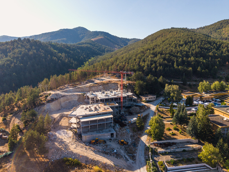 Aerial view of a construction site with a red crane and concrete structures nestled in a forested mountain landscape in Velingrad Pazardzhik Bulgaria. Aerial view of a construction site with a red crane and concrete structures nestled in a forested mountain landscape in Velingrad Pazardzhik Bulgaria.