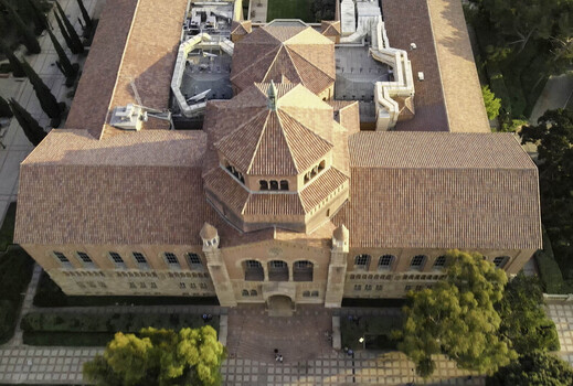 Aerial view of Royce Hall at UCLA Campus featuring its iconic twin towers red tiled roof and Romanesque architecture surrounded by trees and walkways in Westwood California United States.