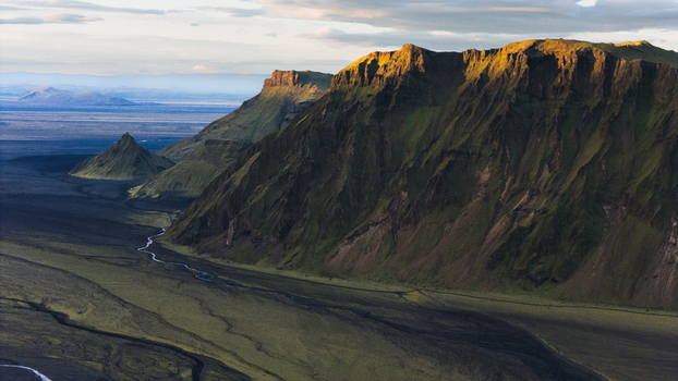 Aerial view of the dramatic green mountains and deep valleys of THakgil with a winding river cutting through the dark volcanic landscape under soft light in Vik Myrdalshreppur Iceland.