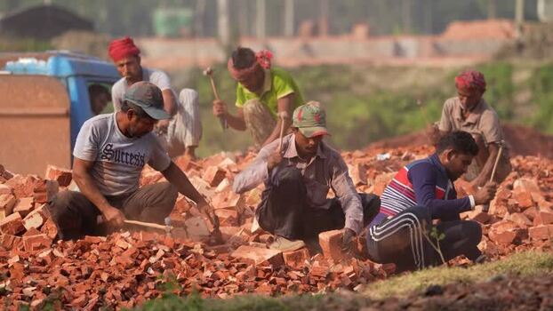 View of men breaking bricks with hammers at a construction site Bangladesh.