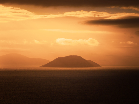 Aerial view of Mistaken Island silhouette during a golden sunset with dramatic clouds over the calm sea in City of Albany Western Australia Australia.