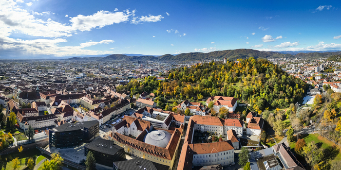 Aerial view of the vibrant red rooftops contrasting with the lush green Schlossberg hill under a bright blue sky Graz Styria Austria.