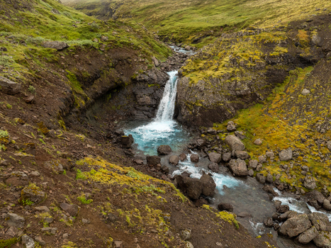 Aerial view of a cascading waterfall flowing through a rocky moss covered valley in the Eastern Region Iceland. Aerial view of a cascading waterfall flowing through a rocky moss covered valley in the Eastern Region Iceland.