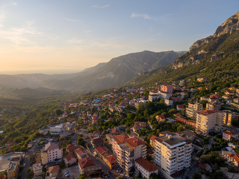 Aerial view of the town of Kruje on a steep mountainside with residential buildings red rooftops and lush green slopes under golden sunset light Kruje Durres County Albania.