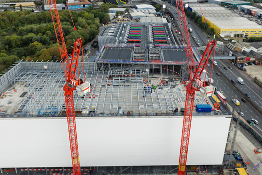 Aerial view of a data center construction site featuring two prominent red tower cranes steel framework and industrial surroundings in the United Kingdom.