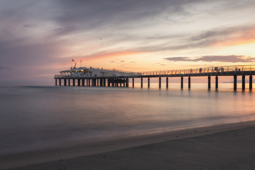 View of the modern pier extending into the sea with people walking at sunset under a colorful sky in Lido di Camaiore Tuscany Italy.