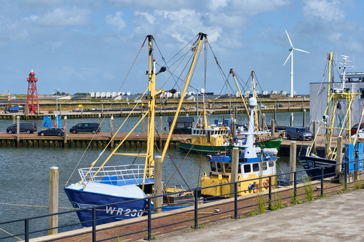 Den Oever Netherlands 20 May 2026 View of fishing boats moored at the Vissershaven harbor with a red beacon and a wind turbine under a cloudy sky. Den Oever Netherlands 20 May 2026 View of fishing boats moored at the Vissershaven harbor with a red beacon and a wind turbine under a cloudy sky.