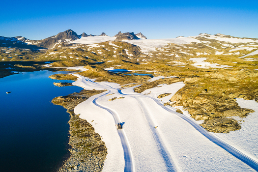 Aerial view of Sognefjellet featuring a glacial lake snow covered mountain terrain and tracks in the snow under a clear blue sky in Lom Municipality Innlandet Norway.