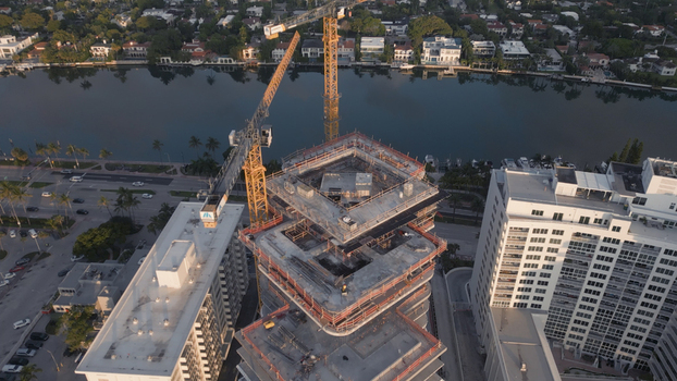 Aerial view of a high rise building under construction with a tall yellow crane surrounded by residential buildings and a canal in Miami Beach Florida United States. Aerial view of a high rise building under construction with a tall yellow crane surrounded by residential buildings and a canal in Miami Beach Florida United States.