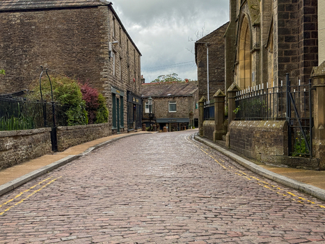 View of a traditional cobbled street lined with historic stone buildings under a cloudy sky in Hawes England United Kingdom. View of a traditional cobbled street lined with historic stone buildings under a cloudy sky in Hawes England United Kingdom.