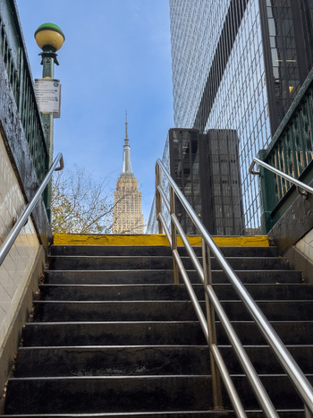 View of the Empire State Building seen from a subway entrance with metal handrails and urban architecture in New York New York United States. View of the Empire State Building seen from a subway entrance with metal handrails and urban architecture in New York New York United States.