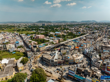 Aerial view of the dense urban landscape of Udaipur featuring busy streets commercial buildings and surrounding hills under a clear sky in Udaipur Rajasthan India.