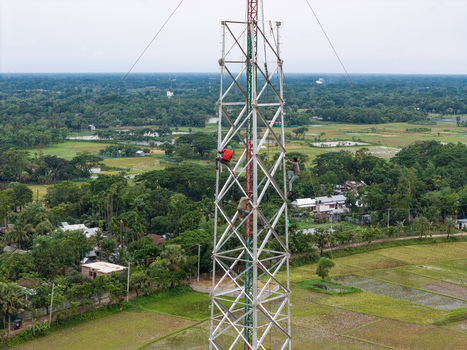 Trishal Upazila Bangladesh 13 May 2026 Aerial view of workers climbing a tall telecommunications tower overlooking lush green rural fields and villages. Trishal Upazila Bangladesh 13 May 2026 Aerial view of workers climbing a tall telecommunications tower overlooking lush green rural fields and villages.