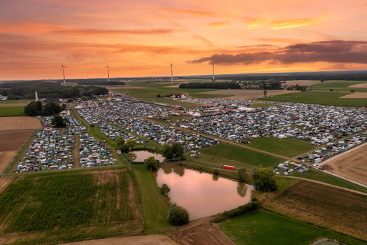 Aerial view of the Open Beatz Festival campsite with tents and cars spread across fields under a sunset sky in Herzogenaurach Bayern Germany. Aerial view of the Open Beatz Festival campsite with tents and cars spread across fields under a sunset sky in Herzogenaurach Bayern Germany.