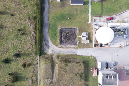 Aerial view of the waste water treatment facility featuring a large white circular tank industrial infrastructure a dirt pit and surrounding grassy fields in Richmond British Columbia Canada. Aerial view of the waste water treatment facility featuring a large white circular tank industrial infrastructure a dirt pit and surrounding grassy fields in Richmond British Columbia Canada.