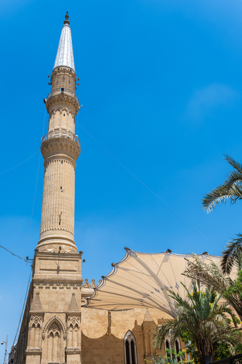 View of the ornate minaret of the Imam Al Hussein Mosque with a large white canopy and palm trees under a clear blue sky in Cairo Egypt. View of the ornate minaret of the Imam Al Hussein Mosque with a large white canopy and palm trees under a clear blue sky in Cairo Egypt.