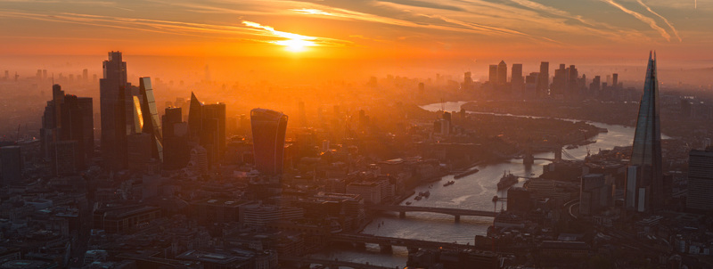 Aerial view of the City of London skyscrapers and The Shard flanking the River Thames under a golden sunrise sky in London England United Kingdom.
