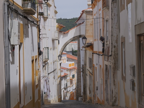 View of a narrow cobblestone street in the historic center with traditional white buildings yellow trim a stone archway and hanging lanterns in Portalegre Portalegre District Portugal.