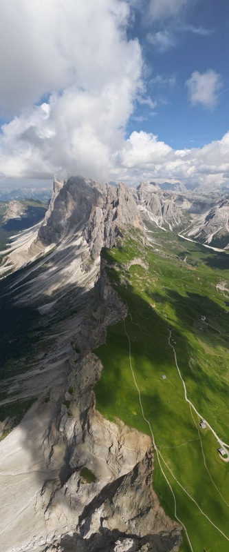 Aerial view of the sharp Seceda ridge in the Dolomite Mountains with green alpine meadows and dramatic rocky cliffs under a cloudy sky Canazei Trentino South Tyrol Italy. Aerial view of the sharp Seceda ridge in the Dolomite Mountains with green alpine meadows and dramatic rocky cliffs under a cloudy sky Canazei Trentino South Tyrol Italy.