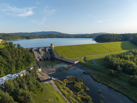 Aerial view of Zapora wodna w Dobczycach dam with a large reservoir lush green embankments and surrounding forests under a clear blue sky in Dobczyce Lesser Poland Voivode Poland.