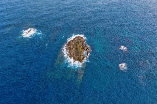 Aerial view of rocky islets and stacks surrounded by deep blue ocean water and white foam near Silence Beach Viewpoint in Cudillero Asturias Spain.