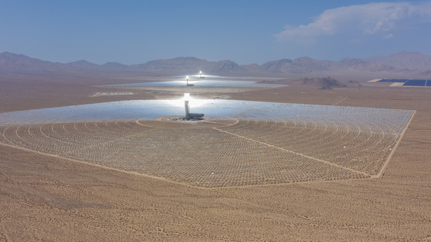 Aerial view of a large concentrated solar power plant with thousands of mirrors and a central solar tower in a desert landscape United States.