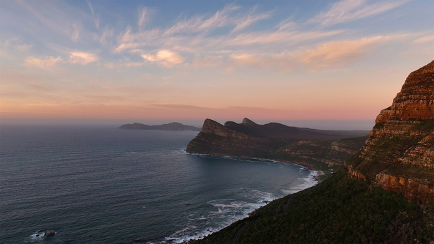 Aerial view of the rugged coastal cliffs and mountains overlooking the Atlantic Ocean under a soft sunset sky in Cape Town Western Cape South Africa. Aerial view of the rugged coastal cliffs and mountains overlooking the Atlantic Ocean under a soft sunset sky in Cape Town Western Cape South Africa.